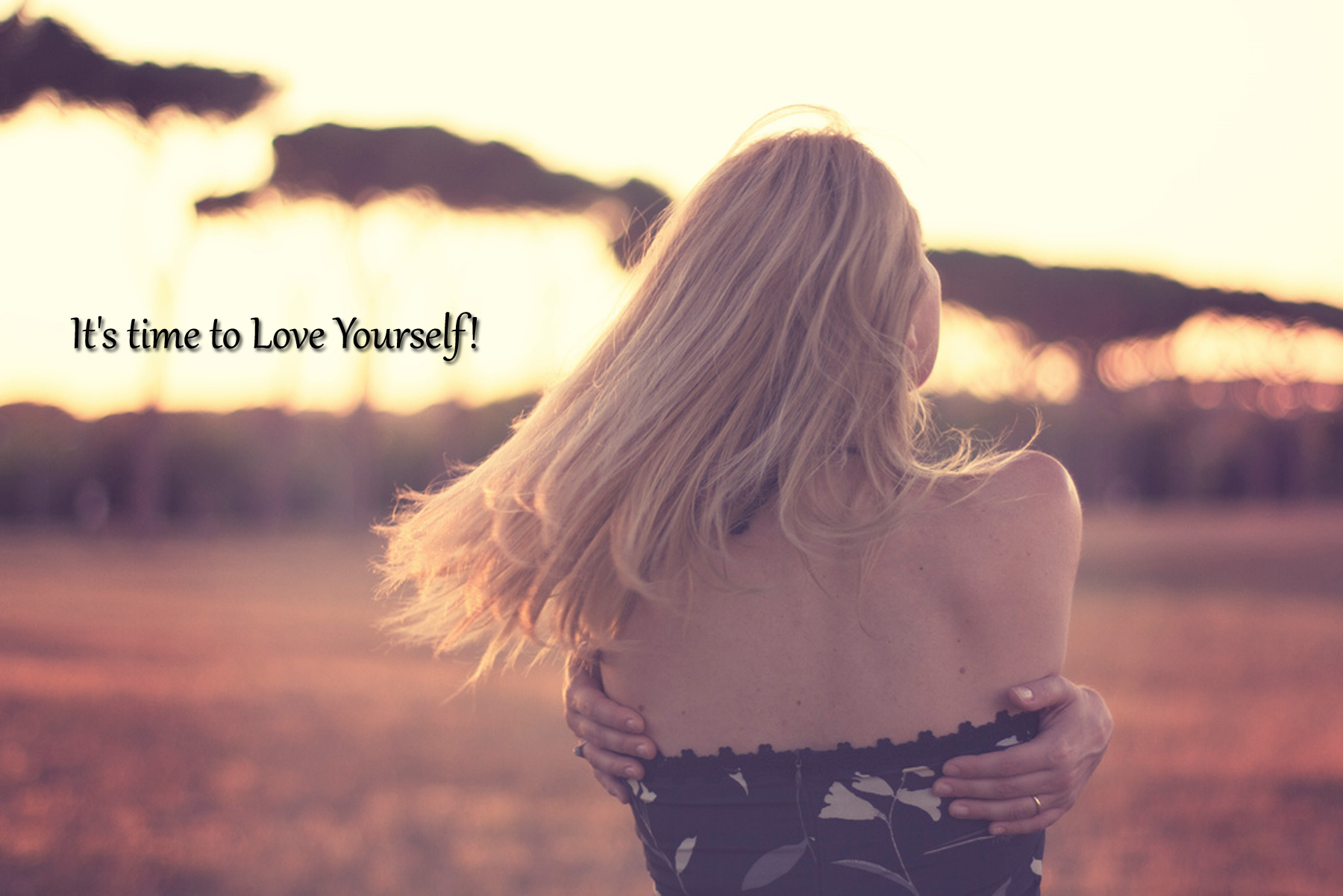 Woman with flowing hair in a sunlit field, embracing herself.